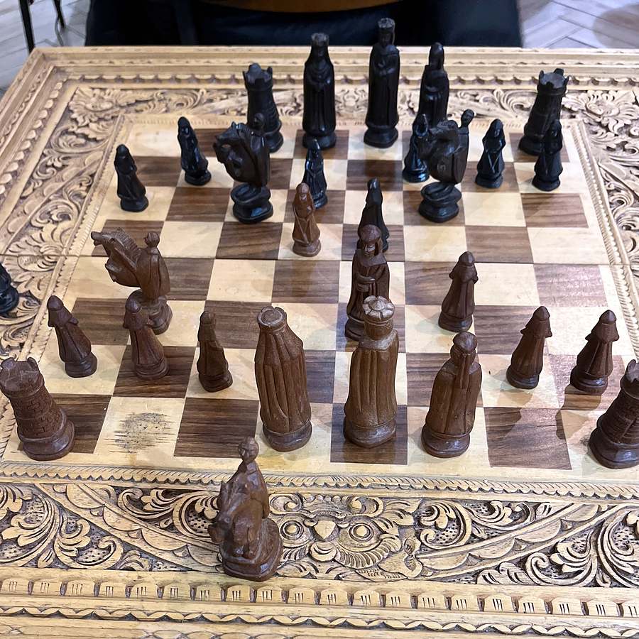 A hand-carved wooden chess set on an ornately carved board, pieces mid-game.