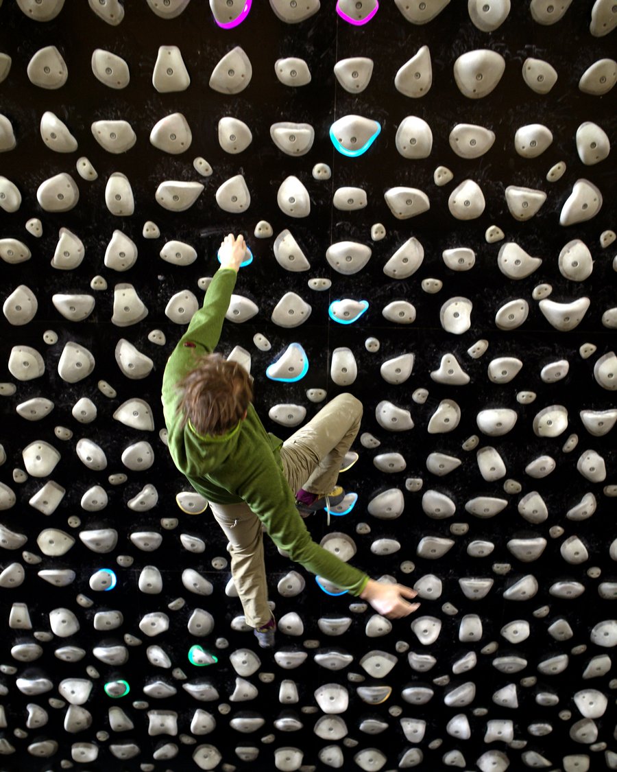 Igor Shatsev mid-move on an indoor bouldering wall, reaching for the next hold.