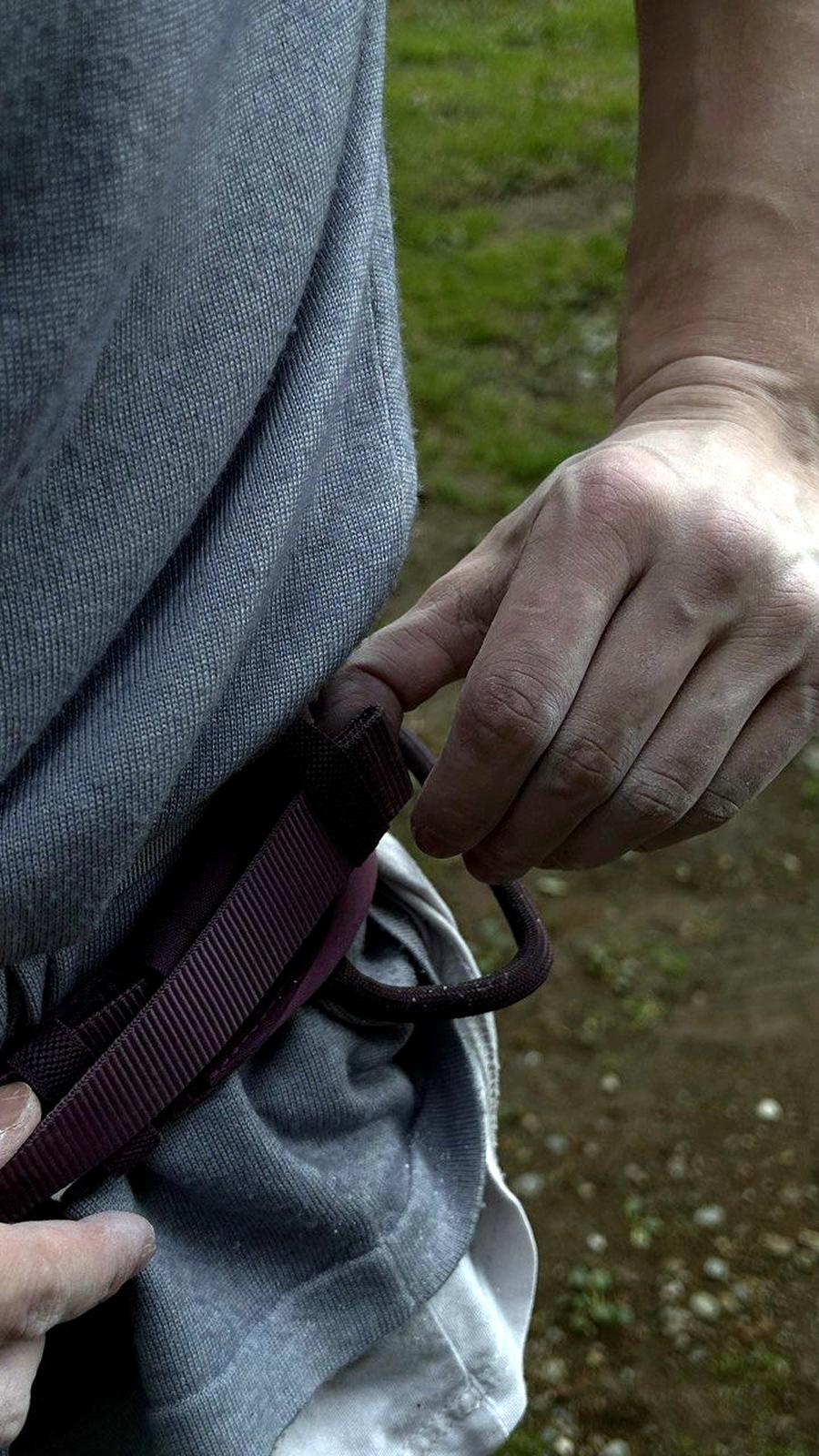A hand at the harness belay loop, threading the rope before a climb.