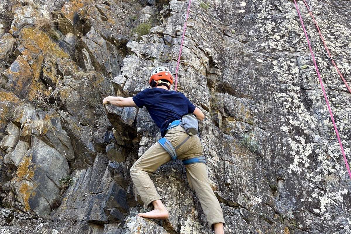 Igor Shatsev climbing an outdoor rock face on a top rope, reaching for a hold.